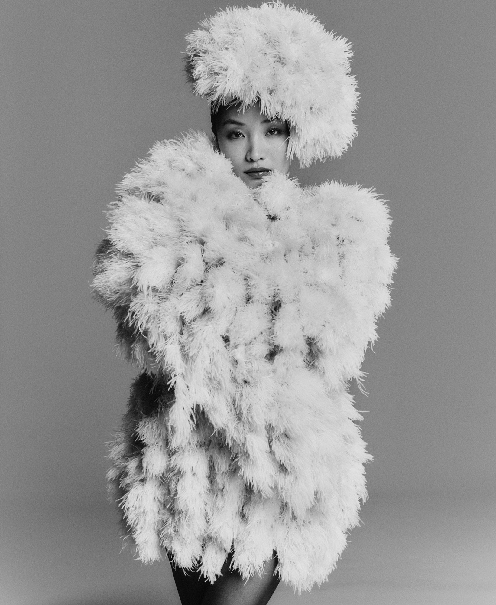 Anna Sawai in a black-and-white Harper's Bazaar studio portrait, wearing a voluminous feathered coat and matching headpiece.